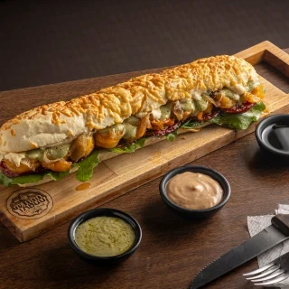 <p>Baguete de Camar&atilde;o com Pesto - Baguete de parmes&atilde;o artesanal, recheada com camar&otilde;es grelhados com tempero exclusivo do Taboo, cream cheese da Casa e pesto &agrave; moda italiana. Acompanha tomate seco, geleia de bacon, alho e cebola caramelizados</p>